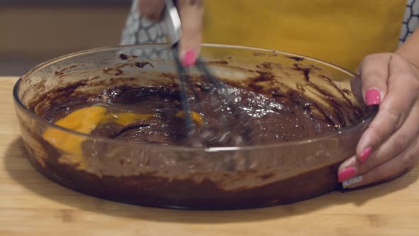 A lady is incorporating the egg into the chocolate batter in a glass bowl