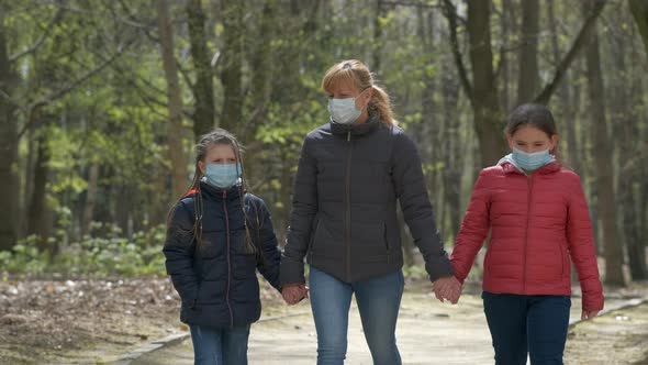 A mother and two daughters walk in a spring Park in medical masks. 