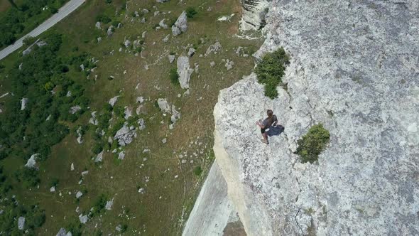 Shooting From Above of a Sporty Man Approaching the Edge of a High Mountain. Extreme Tourist Admires alt