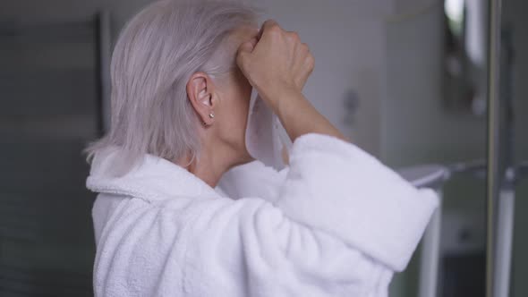Side View Mature Woman Applying Facial Mask Looking in Mirror in Bathroom alt