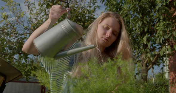 Girl Farmer with a Watering Can Watering Flowers in a Summer Garden at Sunset