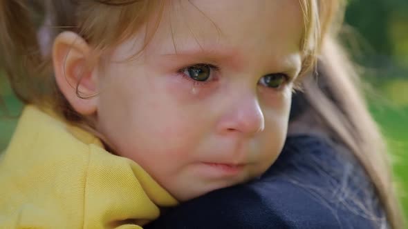 Cose-up portrait of beautiful little two-year-old girl crying in mother's arms