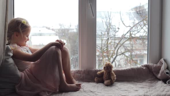 Girl Sitting on a Windowsill with a Teddy Bear