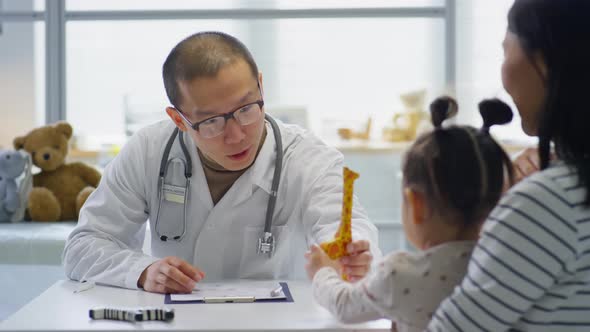 Asian Pediatrician Giving Toy to Little Girl during Consultation alt