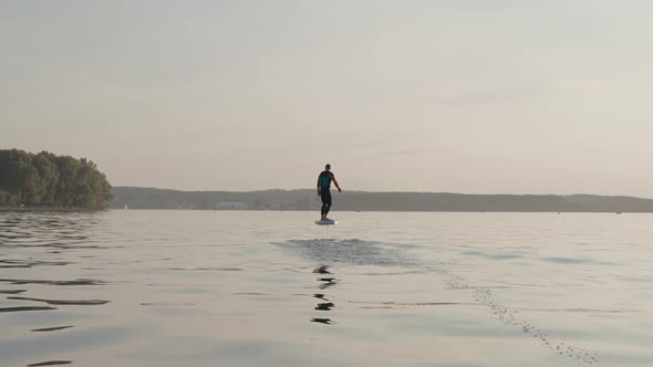Man Riding on a Hydrofoil Surfboard on Large Lake at Golden Sunset alt