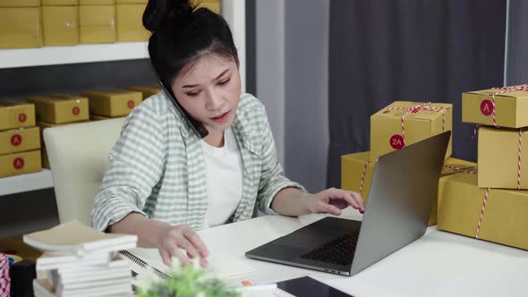 young woman talking on smartphone and use computer laptop to selling product online from home office