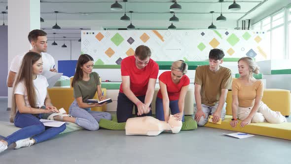 Young Male Practicing CPR First Aid on a Mannequin in the Presence of People alt
