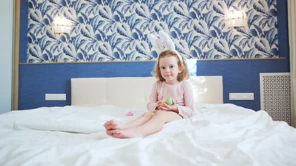 A Cute Little Girl is Sitting on the King Size Bed with Her Legs Stretched Forward alt