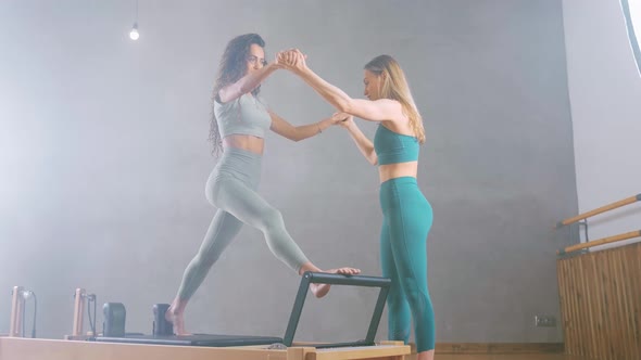 Attractive Fit Woman and Coach in a Pilates Class Working Out on Reformer Machines Doing Leg
