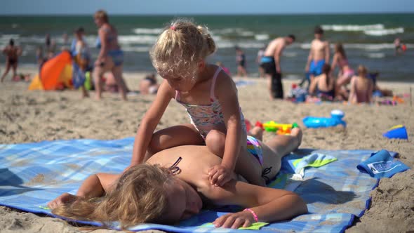 Girl Sitting and Massaging Mother Back on Beach