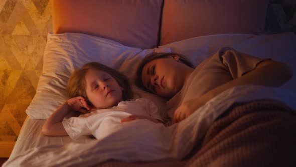 Pretty Little Girl and Mommy Sleep in Wide Bed at Night alt
