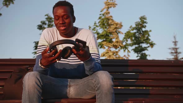 A Young Black Student in Stylish Clothes Sits and Talks on a Smartphone in the City