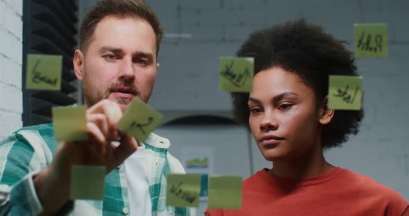 A Young Man and Woman are Planning in the Office Drawing on a Glass Board alt