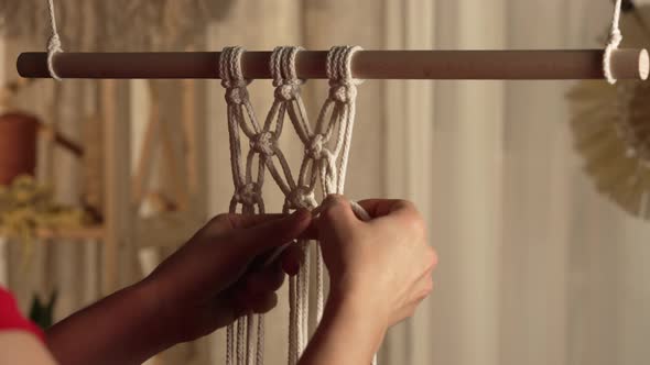 A Woman Craftsman Weaves Macrame From Light Cotton Threads in Her Home Workshop alt