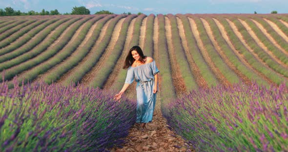 The Beautiful Young Girl Walks Across the Field of a Lavender at Sunset She is Wearing a Long Blue alt