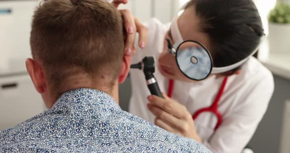Otorhinolaryngologist with Frontal Reflector on Forehead Examining Patient Ear Otoscope  Movie alt
