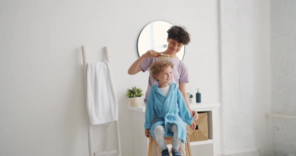 Caring Mother Brushing Curly Hair of Adorable Boy in Bathroom at Home alt