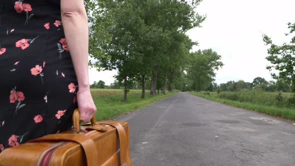 Young girl with suitcase walking down the road on countryside