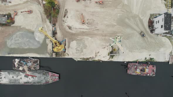 Port cargo cranes on the river bank produce sand. Tractors and excavators in industrial area   alt