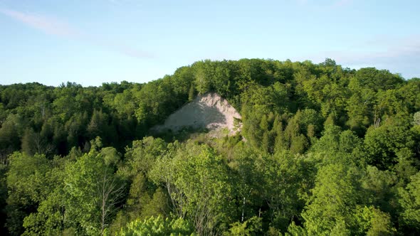 Eroded cliff in densely forested landscape. Crumbling earth and dirt hill cinematic drone reveal fly alt