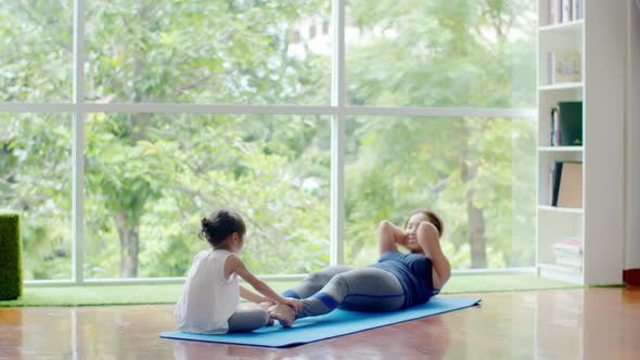 Little girl help her mother doing exercise on fitness mat