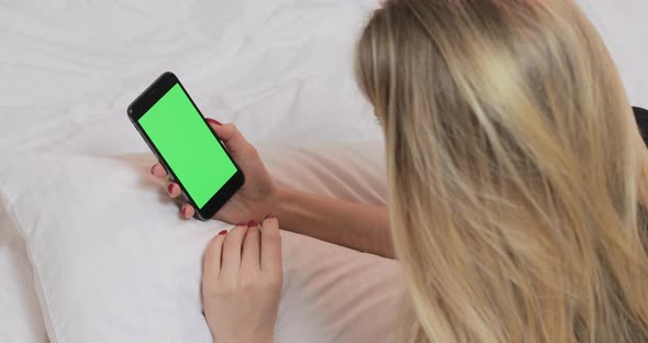 Woman Using Smartphone with Green Empty Screen at the Bed at Home alt
