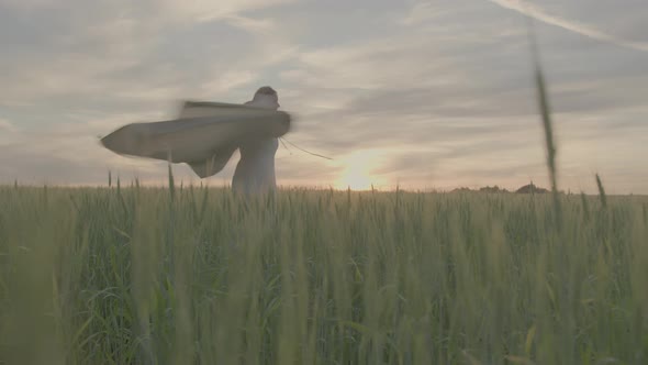 A Young Beautiful Girl in an Ethnic Dress is Spinning in a Green Field of Wheat
