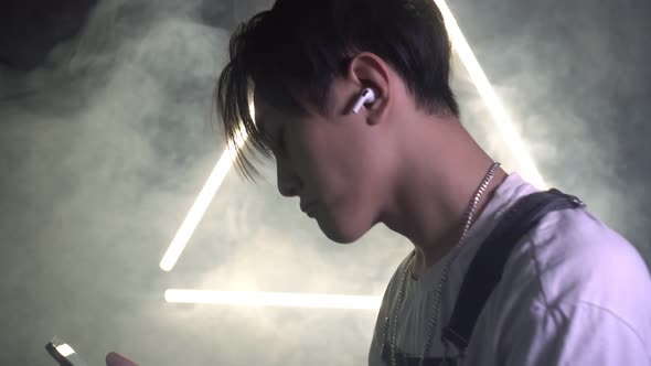 Asian Man Listens to Music in Headphones Using Asmartphone and Dances alt