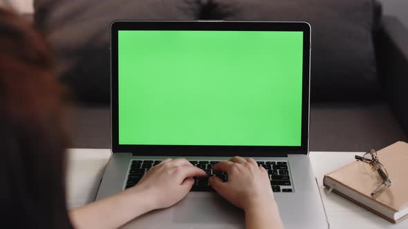 Woman Typing on the Laptop With Green Screen Sitting at the Wooden Table