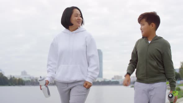 Asian Mother and Son Walking, Chatting and Drinking Water after Run alt