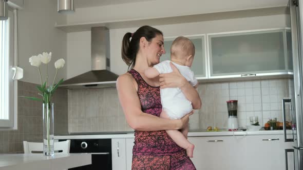 Young mother doing yoga or sport with baby in the kitchen at home alt