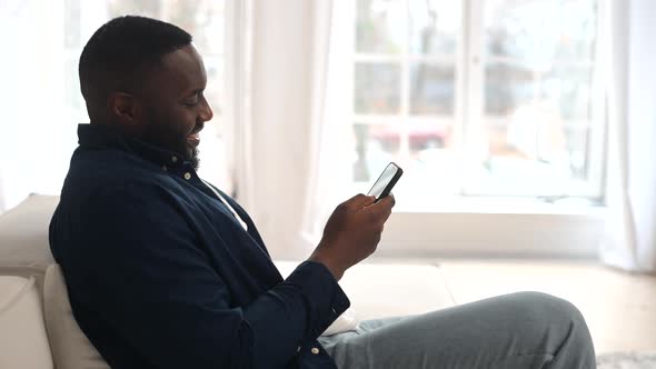 Attractive Millennial Bearded AfricanAmerican Man Relaxing and Sitting on Comfy Sofa alt