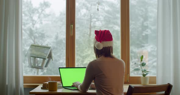 Back View of Girl in Red Santa Claus Hat Typing in Pc Notebook By Window Slow Motion