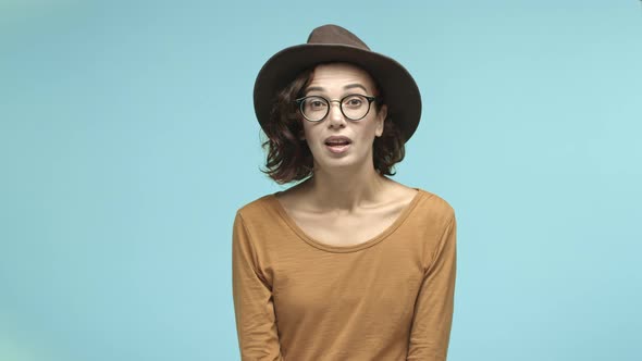 Cute Young Woman in Hipster Glasses and Hat Raising Eyebrows Surprised and Touched Smiling Thankful