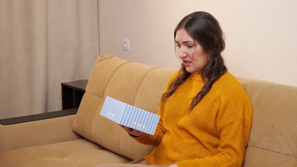 Young Woman Upset About Received Gift Sitting on Sofa alt