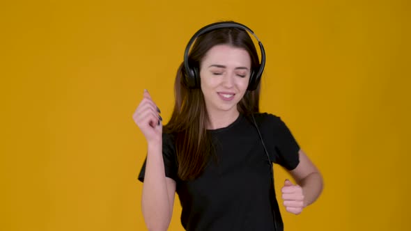Young girl with headphones listens to music and dances isolated on yellow background.