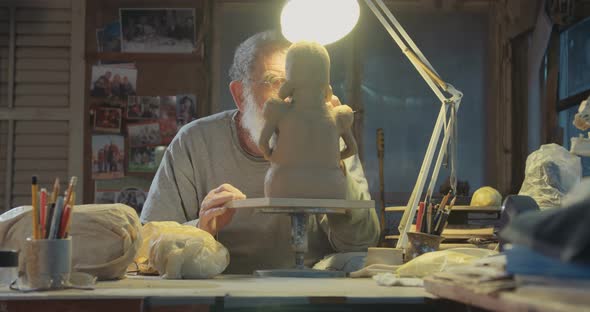Close up of an old sculptor working on a clay sculpture in his small studio alt