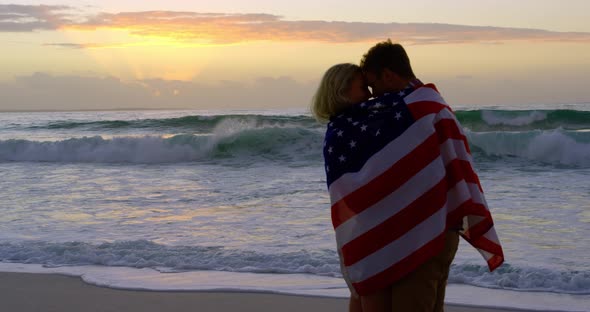 Couple wrapped in american flag at beach during sunset 4k