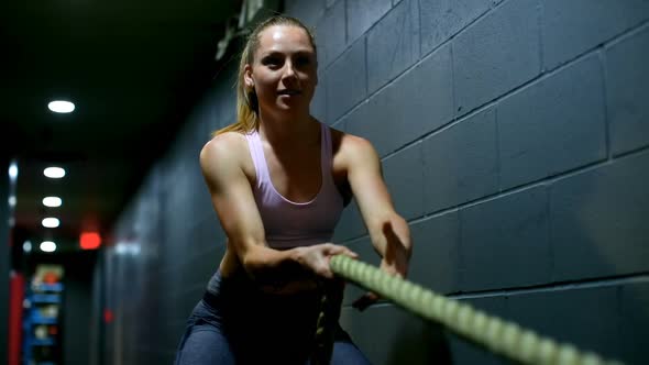 Female athlete exercising with battle ropes in fitness studio