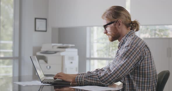 Side View of Handsome Male Entrepreneur Using Laptop Sitting at Desk in Office alt