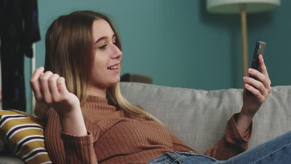 A Young Girl Is Lying on the Couch and Talking on a Video Call