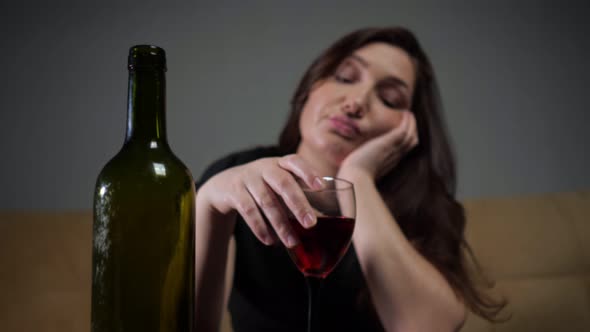 Dark Green Alcohol Bottle Against Blurry Brunette with Depressed Face Expression Drinks Wineglass of alt