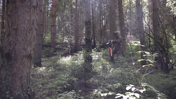 Hunter in Camouflage Aims Gun at Object in the Forest in Summer. Man Hunter Takes Aim with Rifle alt