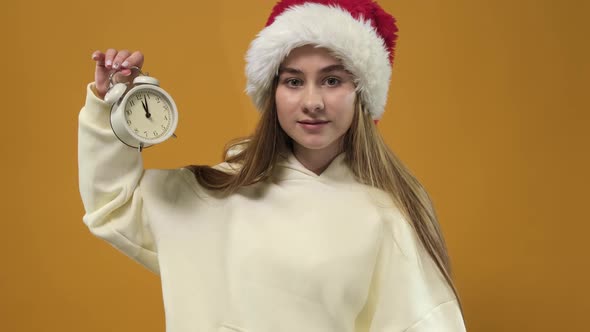 A young woman holding an alarm clock and showing the time.