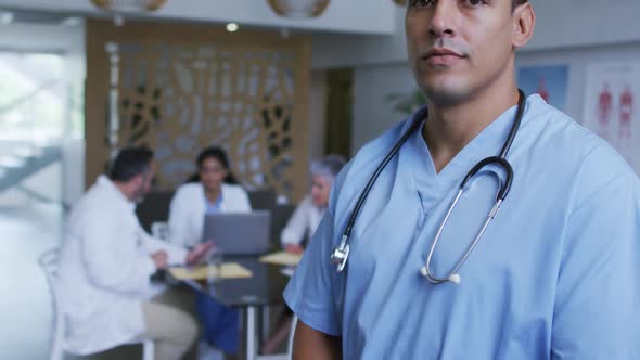 Portrait of mixed race male doctor smiling, with colleagues in discussion in background alt
