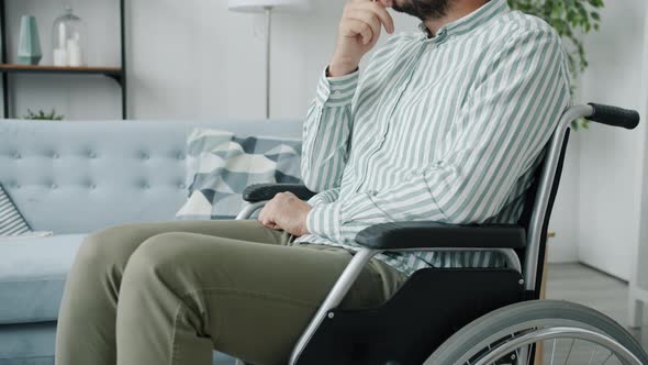 Portrait of Lonely Disabled Guy Sitting in Wheelchair with Sad Face Thinking Indoors at Home alt