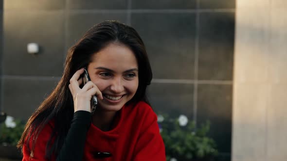 Young Business Lady Talking on a Cell Phone Sitting at a Table in a Cafe on the Street.