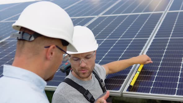 Two Workers in Helmets Check the Installed Solar Panels alt
