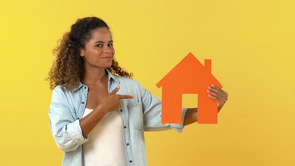 Young African American woman looking at and pointing to house cutout model while acting surprised