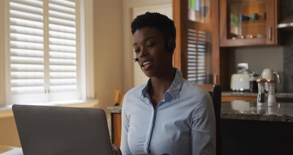 African american woman wearing phone headset having a videocall on laptop while working from home alt